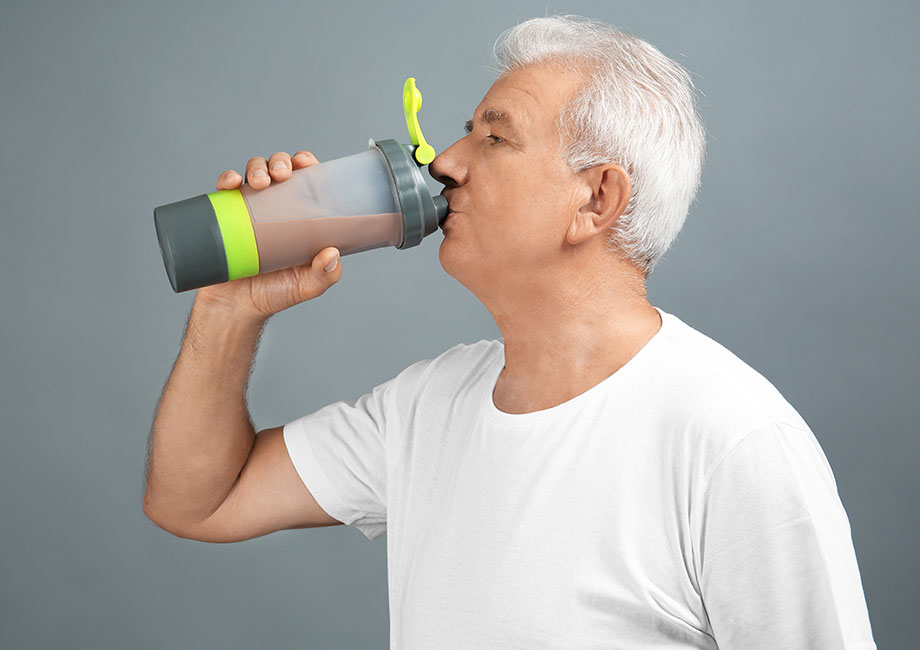 Older man drinking a protein shake from a shaker bottle, promoting healthy nutrition and active living.